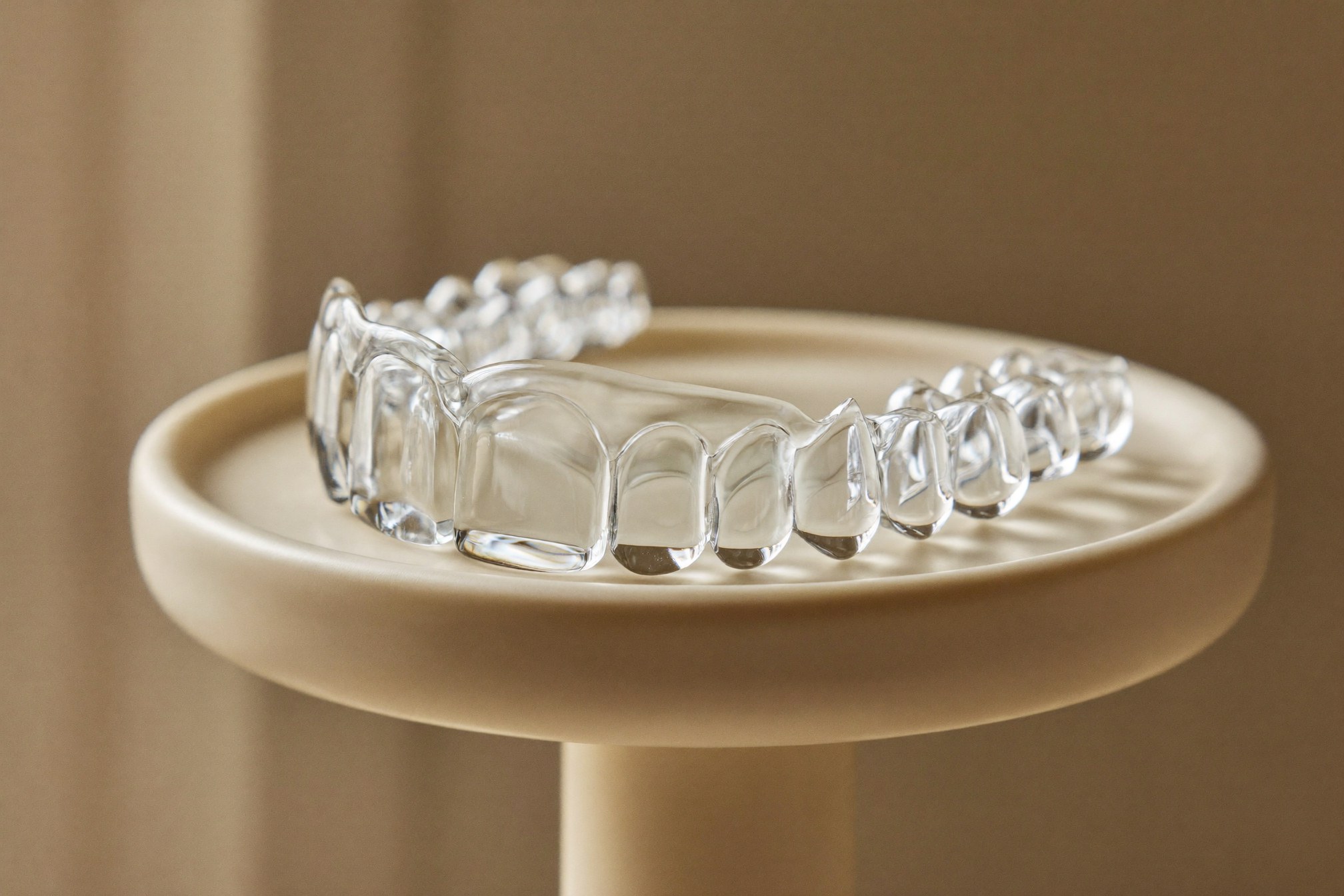 Clear Invisalign aligner on a cream pedestal